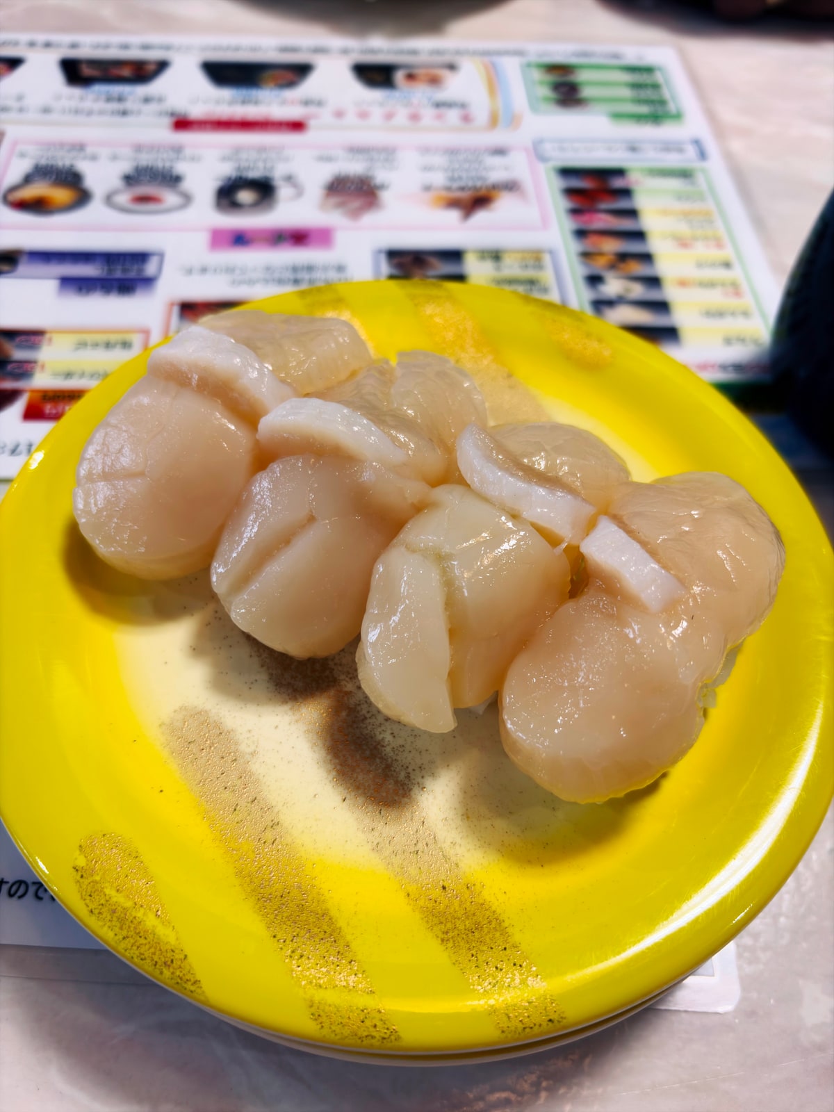 回転寿司の黄色い皿に、帆立の握りが並んでいる。