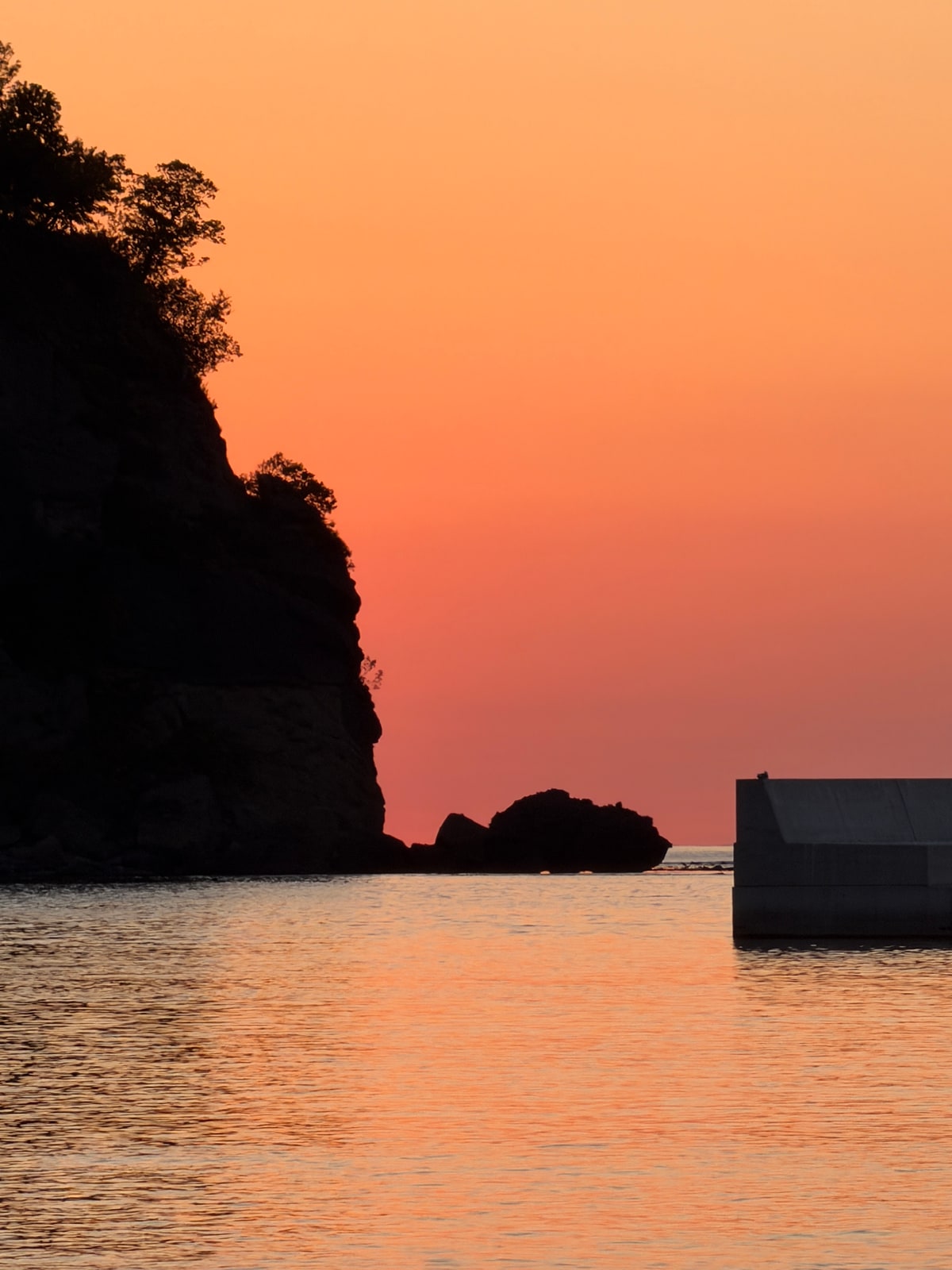 橙色の夕空の下の海。左端に岬の黒い影。