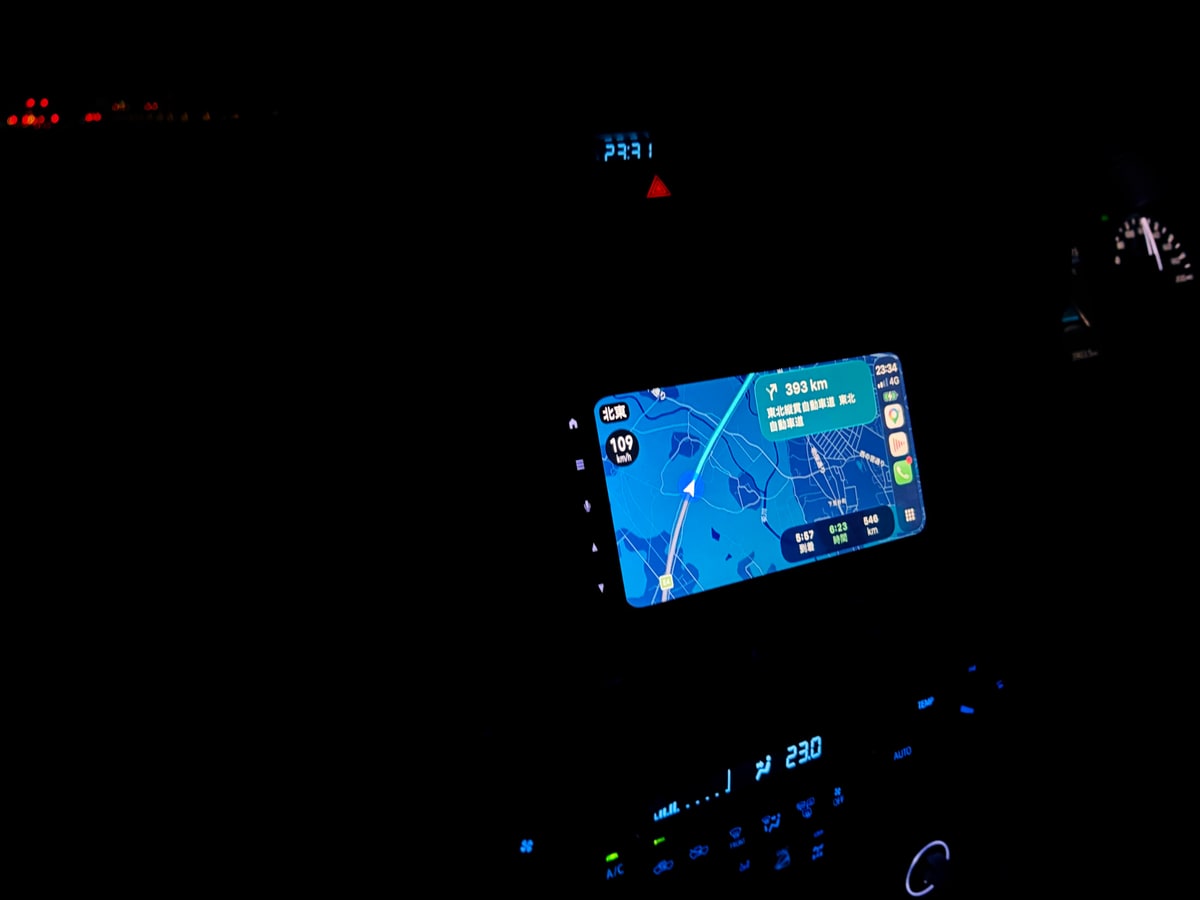 フロントガラス越しの夜の高速道路。二車線の白線が暗がりへ伸び、その上に緑色の標識が小さく光っている。