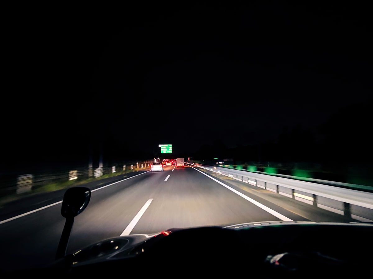 夜の高速道路をボンネット越しに見る。白線と道路照明が暗がりへ続いている。
