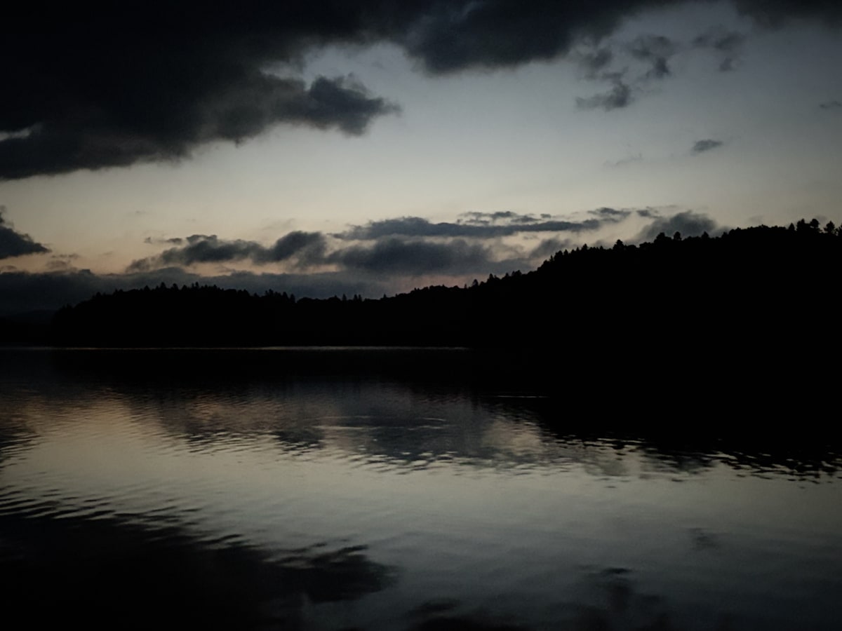夜明け前の湖。横に長い雲の帯の下だけが鈍く光り、森に覆われた島の黒い影が静かな水に横たわっている。