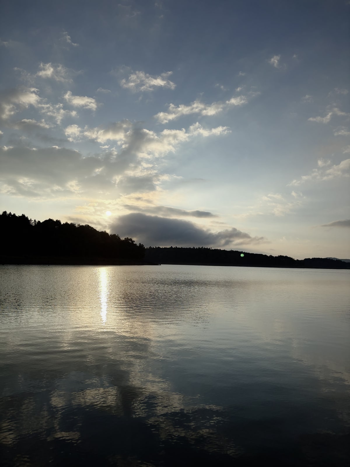 湖の上に厚い雲があり、その切れ目から日が差して水面が白く光っている。向こう岸に低い島。