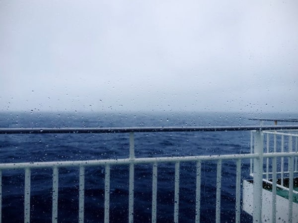 船の白い手摺の向こうに広がる灰色の海。空も同じ灰色で、水平線の位置がはっきりしない。