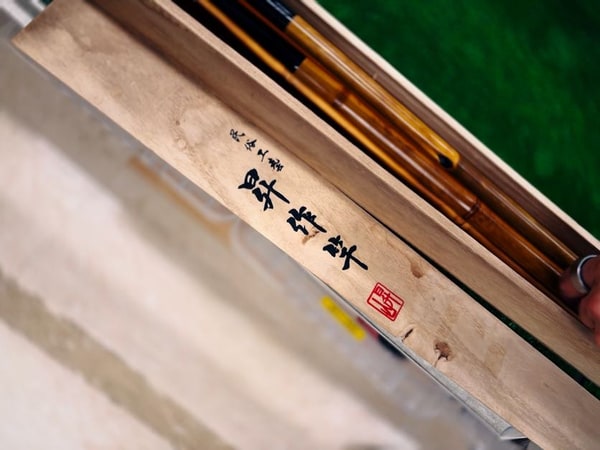 白木の蓋に書かれた墨の字と朱の落款を斜めから写したもの。奥に竹の竿が二本見える。