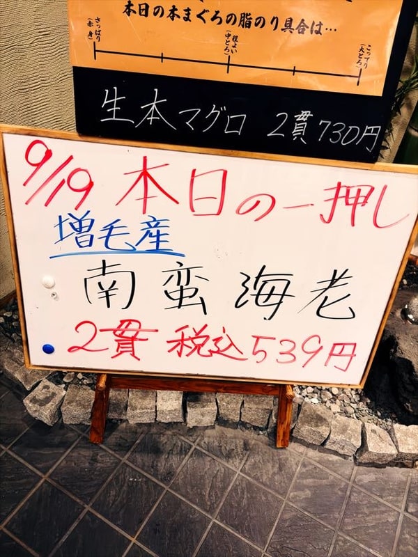 店頭の白い手書きの看板に、日付と本日の一押し、産地と品名と値段が書かれている。上の黒板には鮪の脂の乗り具合を示す目盛りがある。