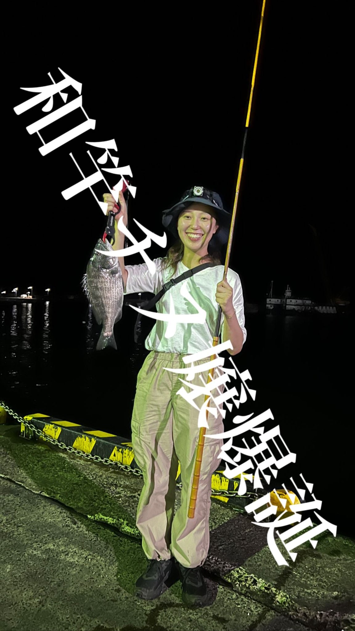 夜の岸壁で、延べ竿とチヌを掲げるチヌ嬢